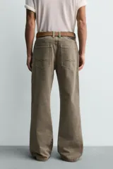 Pantalón de denim color verde oliva, estilo chino con corte ancho y bota acampanada (flare) desde la rodilla. Tiro medio, confeccionado en tejido rígido. Presenta bolsillos frontales y bolsillos traseros de plastrón.