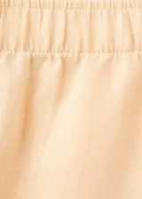 Pantalón de lino color beige, de diseño recto y largo con tiro medio, dos bolsillos laterales y cintura ajustable.