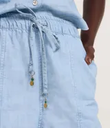 Short runner de mezclilla color celeste, con cintura alta, elástico y lazo ajustable que incluye colgantes decorativos de piña, además de bolsillos estilo carpintero.
