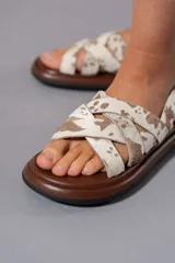 Sandalias chatas con base marrón y tiras cruzadas de cuero con estampado animal print de vaca.