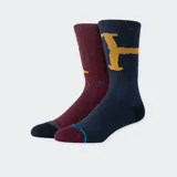 Pack de dos pares de medias Stance con diseños de Harry Potter. Un par es color borgoña con motas y el logo de Stance en amarillo. El otro par es azul marino con motas y un diseño de una escoba dorada.