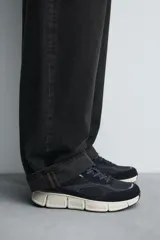 Zapatilla deportiva azul marino con detalles en gris oscuro y blanco. La parte superior está fabricada en combinación de piel con acabado serraje y tejido técnico transpirable. Cuenta con una suela ligera y voluminosa.