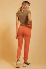 Pantalón de corte recto y tiro alto, color naranja, con bolsillos laterales y cierre frontal con botón y cremallera. Incluye un cinturón fino de cuero marrón.