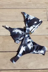 Conjunto de bikini con estampado tie-dye en tonos negro y blanco. El top es de estilo triángulo fijo con breteles regulables y cierre de gancho en la espalda. La bombacha es de corte vedetina con laterales fruncidos elásticos.