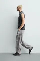 Pantalón de jean estilo carpintero con corte relaxed fit, tiro medio y pierna recta. Presenta un lavado azul medio con efecto desgastado y roturas en las rodillas. Incluye bolsillos laterales tipo plastrón, tira multifunción en la pierna, cierre frontal con cremallera y botón.