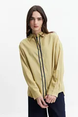 Camisa oversize color crema con detalles de puntilla roja en el frente.