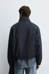 Cazadora de corte cropped confeccionada en tejido de algodón con ligero acolchado interior. Presenta cuello subido, cierre frontal con cremallera, mangas largas con puños elásticos y bolsillos laterales de vivo.