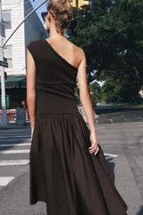 Vestido midi negro con escote asimétrico de un solo hombro, cuerpo ajustado y falda amplia de corte asimétrico con frunces en la cintura.