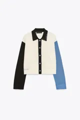 Chaqueta de punto de manga larga con cuello solapa y cierre frontal de botones. Presenta un diseño de bloques de color: cuerpo principal color crema, manga izquierda negra, manga derecha azul claro y cuello negro. Incluye detalles de costura expuesta en azul claro en el cuello y el bajo.