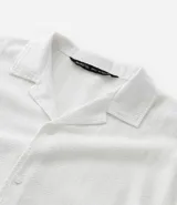 Camisa de corte boxy fit, color blanco, con cuello bowling, cierre frontal con botones y manga corta. Confeccionada en tejido de algodón con textura jacquard.
