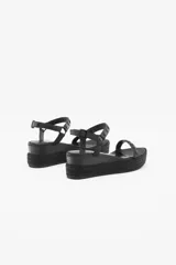 Sandalia negra con plataforma forrada en yute trenzado, de doble tira. La tira de la capellada está confeccionada en cuero con tachas texturadas y lisas de acabado níquel, mientras que el tobillo se sujeta con una segunda tira de cuero con las mismas tachas y hebilla metálica con grabada de la marca. Cuenta con una suela de caucho para mayor confort.