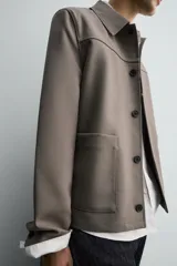 Sobrecamisa de corte relajado confeccionada en tejido compacto con lana. Presenta cuello solapa, cierre frontal con botones, mangas largas con puños abotonados y dos bolsillos de plastrón en la parte frontal.
