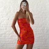 Vestido corto de microtul con diseño drapeado, escote strapless y estampado floral en tonos naranja y fucsia.