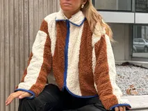 Campera de corderito con diseño de bloques de color, confeccionada en tejido sintético de textura suave. Presenta cierre frontal, cuello alto y ribetes en contraste en los bordes.