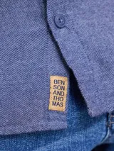 Camisa de manga larga en tono azul jaspeado, con cuello clásico, cierre frontal de botones y un bolsillo en el pecho.
