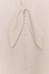 Blusa de cuello subido con escote en pico y cierre frontal con botones forrados. Presenta mangas abullonadas de largo tres cuartos con elástico en los puños y detalle de lazos en el cuello y el frente.