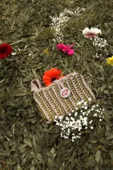 Bolso de mano tejido a crochet en trapillo grueso color verde oscuro, con un botón metálico grande y redondo con el logo de la marca CAPER en rojo.