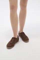 Zapatillas de estilo urbano color chocolate, confeccionadas en material textil tipo gamuza, con cordones al tono y suela de goma plana.
