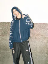 Hoodie con cierre frontal, tejido en algodón con diseño reversible. Presenta detalles de roturas intencionales en puños, ruedo y costuras, con estampado gráfico en mangas y capucha.