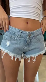 Short de jean tiro bajo, color celeste claro, con roturas y terminación deshilachada en el ruedo. Presenta un lavado desgastado y costuras visibles.