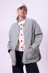 Campera acolchada color gris claro, con cuello mao y cierre frontal con botones a presión. Tiene bolsillos laterales y corte holgado.