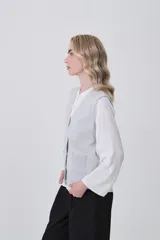 Chaleco de punto gris con escote en V, cierre frontal de botones y dos bolsillos delanteros con terminación acanalada.