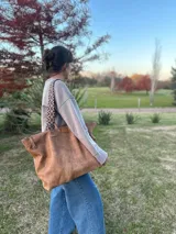 Bolso grande tipo tote de cuero color marrón gastado, con doble asa corta de madera y correa larga de tela estampada.