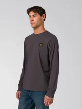 Remera de manga larga color gris oscuro, con cuello redondo y puños acanalados. Presenta un pequeño parche rectangular con el logo de la marca en el lado izquierdo del pecho.