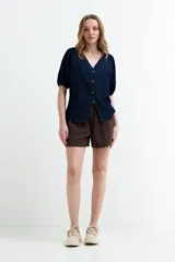Blusa de denim oscuro con cuello en V, cierre frontal de botones y mangas cortas abullonadas con puños elastizados.