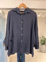 Camisa oversize de lino color azul marino, con cuello camisero, cierre frontal de botones claros, mangas largas y bolsillo aplicado en el frente.