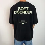 Remera negra de corte oversize con estampado gráfico en la espalda que incluye el texto 'SOFT DISORDER' en color verde claro y detalles adicionales con la frase 'FOUNDED TO FEEL, NOT TO FOLLOW'.