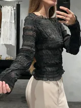 Remera de manga larga en tejido semitransparente color negro, con diseño de frunces horizontales en todo el cuerpo y las mangas, y terminaciones con volados sutiles.