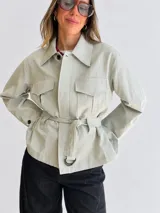 Campera verde claro de algodón, con cuello amplio, bolsillos delanteros con solapa, cierre frontal con botones y cinturón ajustable del mismo género con hebilla metálica.