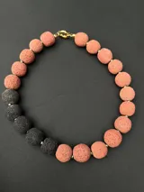 Collar de piedras volcánicas naturales con diseño de esferas texturizadas en tonos rosado y gris oscuro, dispuestas de forma asimétrica.