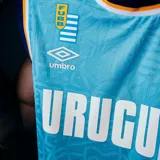 Camiseta de básquet Umbro de la selección uruguaya, color celeste con detalles en azul y blanco. Presenta estampado frontal con la palabra Uruguay, logo de la marca y sponsor Antel.