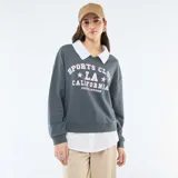 Buzo de cuello redondo color gris oscuro con estampa frontal estilo universitario en color blanco. Presenta un diseño de doble capa con cuello y ruedo de camisa blanca incorporados, mangas largas con puños elásticos y corte holgado.