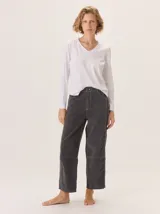 Pantalón de pana color gris oscuro, de corte barrel (holgado en caderas y muslos, ligeramente afín hacia el tobillo). Presenta costuras visibles en contraste de color amarillo claro, especialmente en la zona de la rodilla y el ruedo.