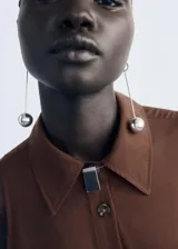 Vestido midi de color marrón, con diseño evasé, cuello camisero y cierre frontal con botones. Presenta un cinturón ajustable a la cintura y un diseño sin mangas con tirantes anchos.