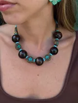 Collar corto con cuentas de madera color marrón oscuro, cuentas tibetanas con incrustaciones de color turquesa y detalles en metal color bronce. Cierre con cadena de acero quirúrgico y gancho para regular el largo.