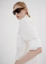 Camisa blanca de corte recto con mezcla de algodón y lyocell, adorno de perlas, cuello camisero, manga larga con puños abotonados y cierre delantero con botones ocultos.