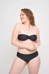 Corpiño strapless negro con copa fija y ballenas laterales, con detalle de ribete blanco en el borde superior e inferior. Incluye bretel desmontable y broche de ajuste en la espalda.