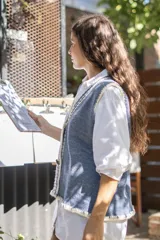 Chaleco tejido de punto color azul con destellos de lurex, escote en V y cierre frontal con botones. Presenta detalles de bordado artesanal en lana blanca en los bordes y terminaciones en crochet.