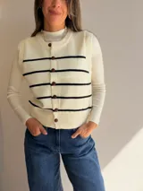 Chaleco tejido de punto con diseño de rayas horizontales negras sobre fondo blanco. Presenta cuello redondo, cierre frontal con botones y terminaciones en tejido acanalado.