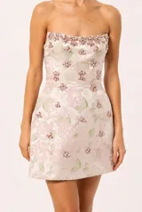 Vestido corto strapless de Patbo en tono rosado con estampado floral en jacquard, adornado con aplicaciones bordadas de pedrería en forma de flores que aportan brillo y textura.