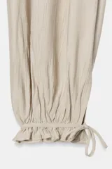 Pantalón bombacho color beige de tiro medio con cintura elástica, bolsillos delanteros y bajo acabado en puño con lazada.