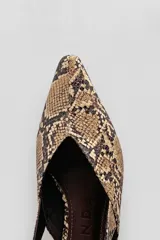 Zapato tipo flat destalonado de color negro con acabado brillante, punta fina y cierre con hebilla lateral.