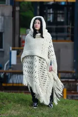 Poncho tejido a mano en lana merino color crudo, con capucha, cuello alto y flecos.