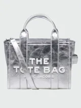 Bolso tote pequeño Marc Jacobs confeccionado en cuero metalizado plateado con acabado arrugado. Presenta el logo distintivo "THE TOTE BAG" en relieve blanco en el frente, doble asa superior y correa ajustable extraíble.