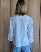 Blusa rosada de algodón con delicados bordados florales blancos, escote en V con cuello elevado y volados, y mangas largas con puños acampanados.