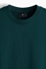 Remera en punto de algodón verde oscuro, con cuello redondo ribeteado, hombros caídos, mangas cortas y bajo recto de corte relajado.
